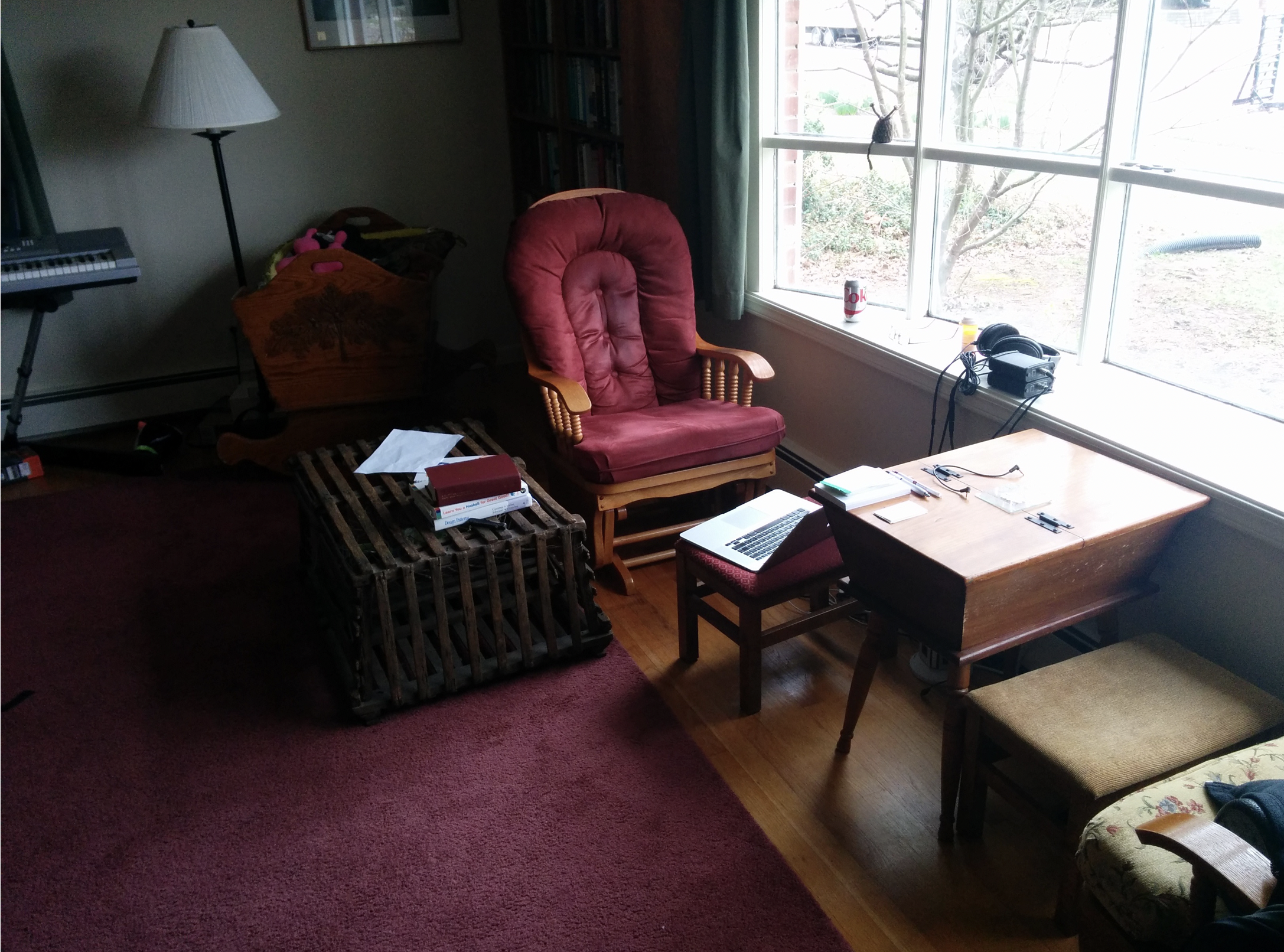 We are looking toward a chair. On our right is a bay window. In front is a low table. To the left is a lobster trap with books on it.